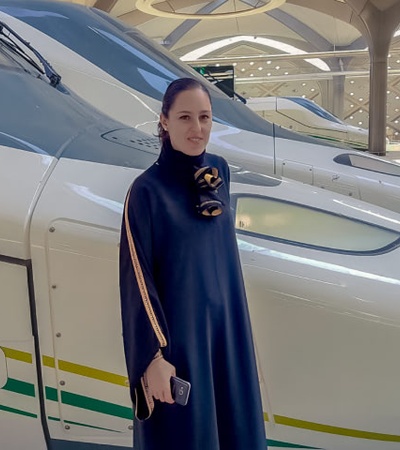A woman standing in front of two high-speed trains at a station.