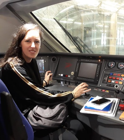 A woman sitting at the control panel inside a train cockpit.