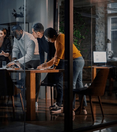 A group of five professionals actively discussing around a table in a modern office environment at night.