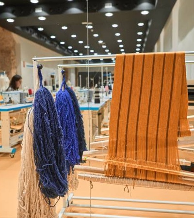 A well-lit textile workshop with various looms and colorful yarns hanging.