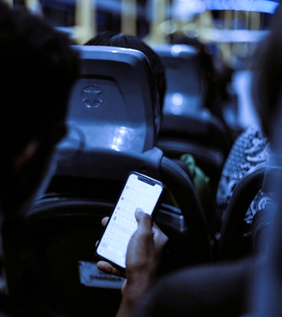 A person using a smartphone on a bus at night, with other passengers visible in the background.