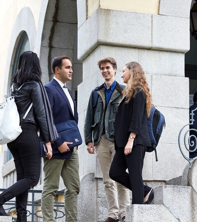 A group of four young adults engage in conversation while standing on steps of a building.