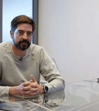 A man sitting at a desk in an office, talking, with subtitles on the video screen.