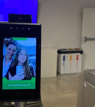 A digital display showing a selfie of a couple at a security checkpoint with a greeting message.