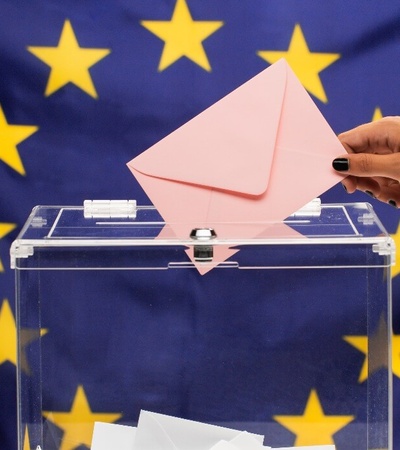 A person casting a vote into a ballot box with a European Union flag background.
