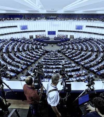Photographers capturing a session in a large semi-circular parliamentary chamber filled with seated attendees.