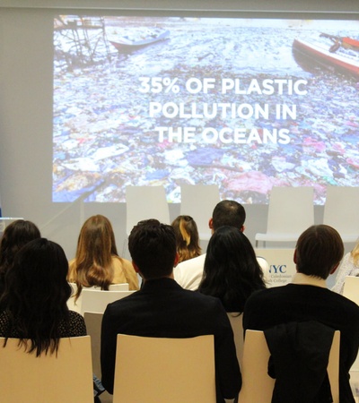 A presentation on ocean pollution taking place in a conference room, featuring flags of Finland and the USA.
