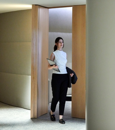 A woman walking through a modern office hallway, holding a laptop.
