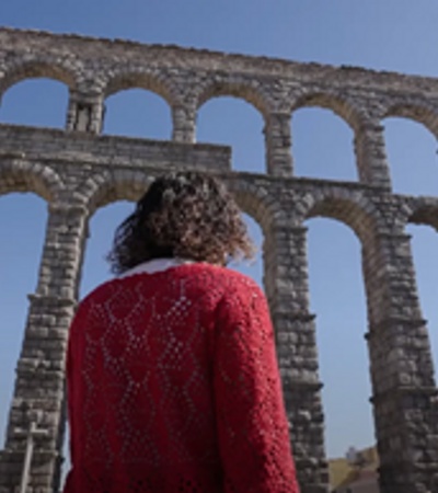 A person stands in front of an ancient aqueduct under a clear blue sky.