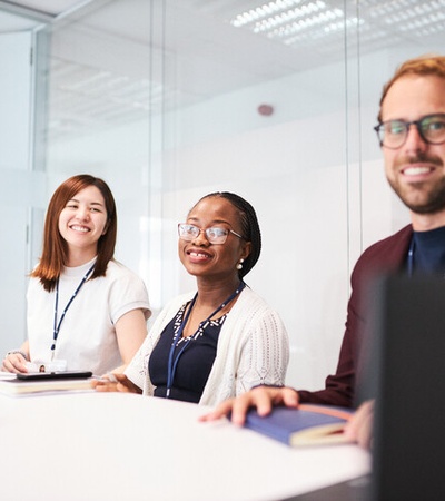 A group of three smiling people at a conference table in a modern office setting.