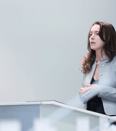 A woman in a blue suit is speaking at a podium in a business or academic setting.