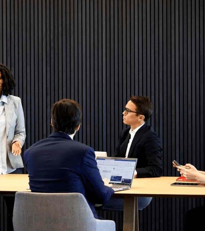 A business meeting with five professionals around a table in a modern office setting.