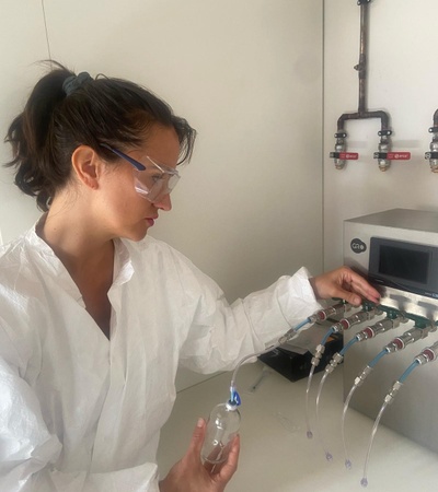 A woman in protective gear is operating a scientific apparatus with multiple tubes and valves.