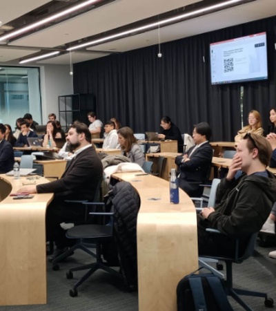 A group of people sitting in a modern classroom listening to a presenter at the front.