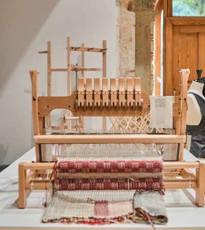 A traditional wooden weaving loom displayed in a room with a mannequin wearing a black garment.