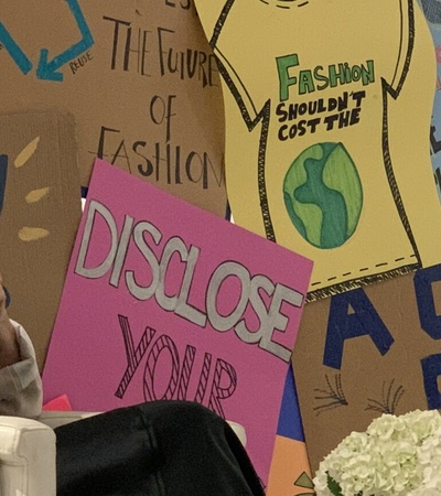 Two women seated in front of colorful protest signs, engaging in a discussion at a public event.