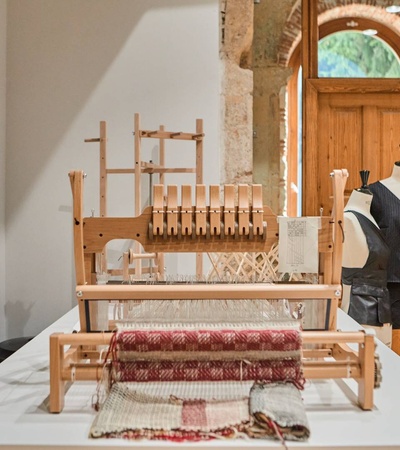 A traditional wooden weaving loom and a mannequin dressed in period clothing displayed inside a historic setting.