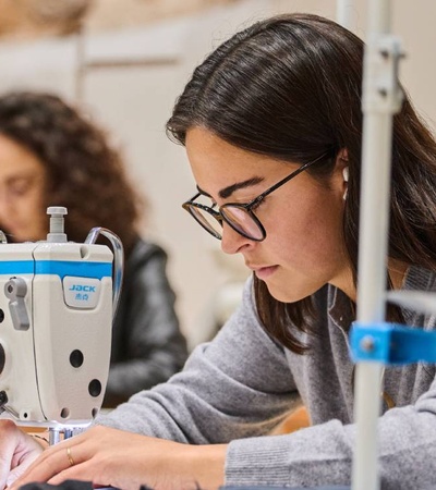 A woman is sewing fabric with a sewing machine in a workshop setting.