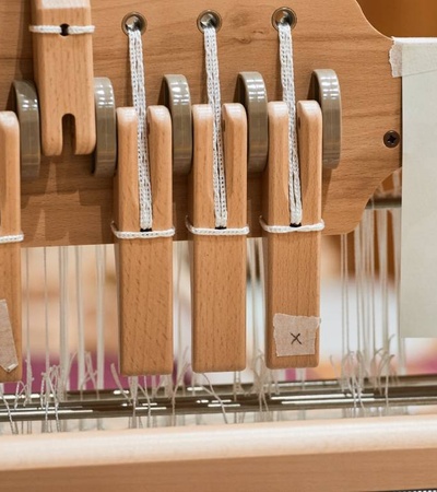 A close-up view of a loom showing wooden levers and tensioned threads.