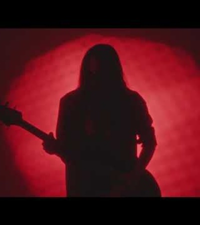 Silhouette of a person playing guitar against a red circular background