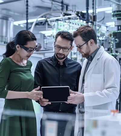 Three professionals are collaborating on a tablet in a modern lab environment.