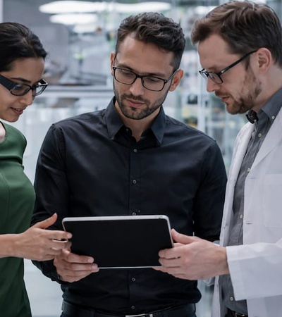 Three colleagues in a laboratory are discussing data on a tablet.