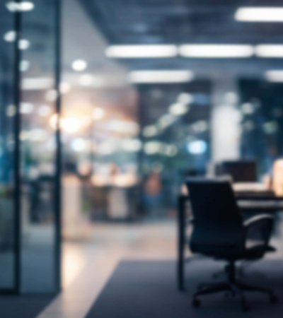 A blurred image of an office interior with a chair and desks in the background.