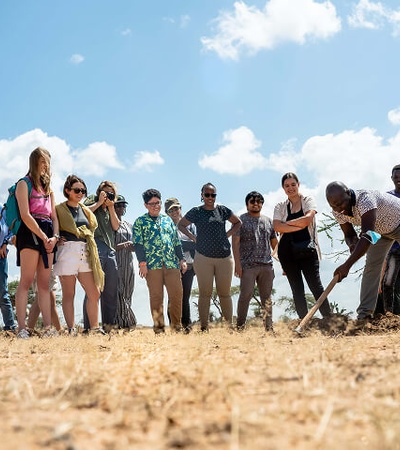 A group of people observing a man working on the ground in an outdoor setting.