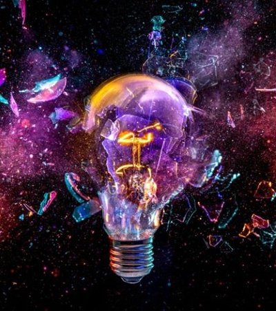 A shattered light bulb emits colorful sparks within a cosmic background.
