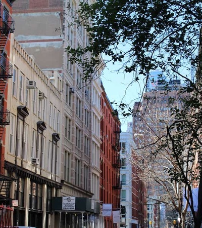 A quiet street in a city with historic buildings and a glimpse of a tall modern skyscraper in the distance.