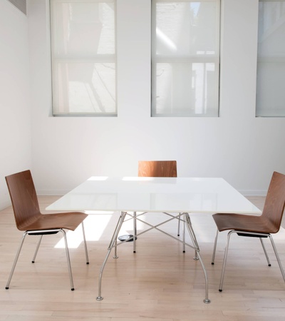 A bright and minimalistic meeting room with a white table, three chairs, and large windows.