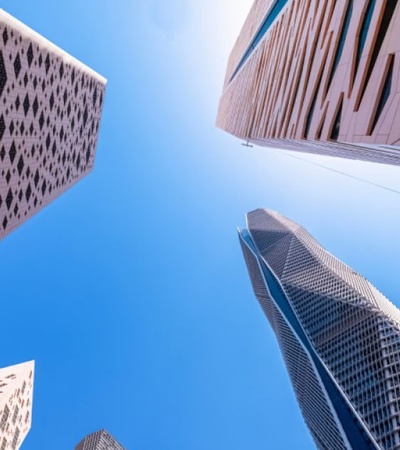 Looking up at the sky surrounded by towering skyscrapers under a clear blue sky.