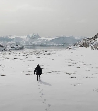 A person walking through a snowy landscape with icebergs in the background.