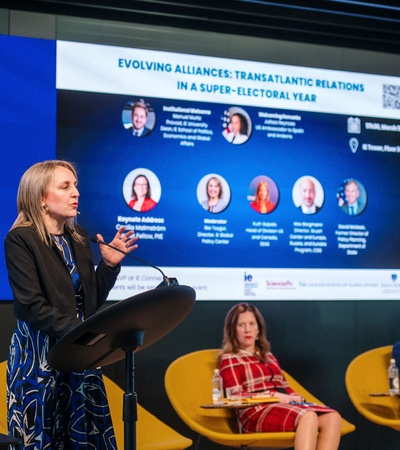 A woman is giving a presentation at a podium in front of an audience at an event titled 'Evolving Alliances: Transatlantic Relations in a Super-Electoral Year' at IE University.