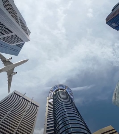 A plane flying above tall skyscrapers under a cloudy sky.