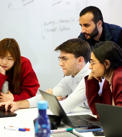 A group of young people collaboration on laptops in a modern workspace.