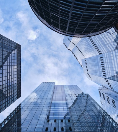 Looking up at a cluster of modern skyscrapers under a clear blue sky.