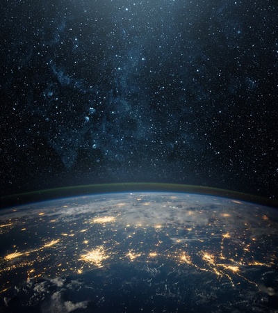 A panoramic view of the Earth from space showing the planet at night with city lights glowing and stars in the background.