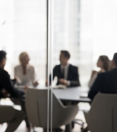 Blurred image of a group of professionals in a meeting around a table in a modern office.