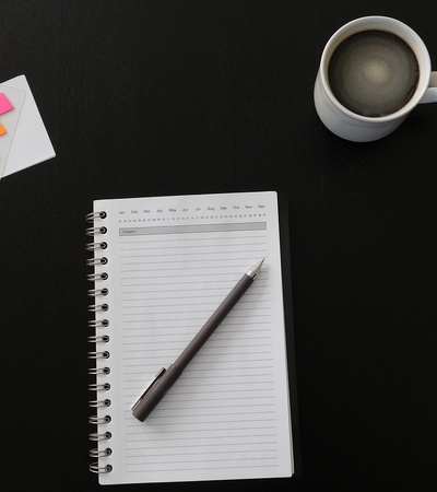 A neat workspace featuring a notepad with a pen, colorful sticky notes, a cup of coffee, and a computer mouse on a dark surface.