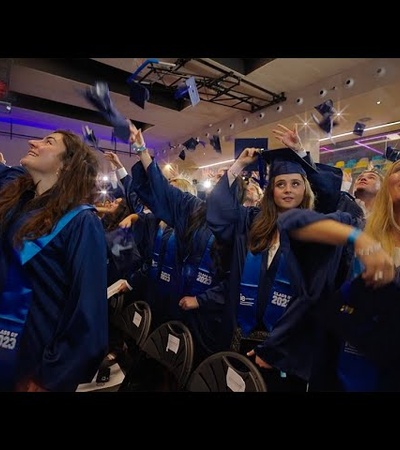 Graduates in blue gowns joyfully throwing their caps in the air during a graduation ceremony.