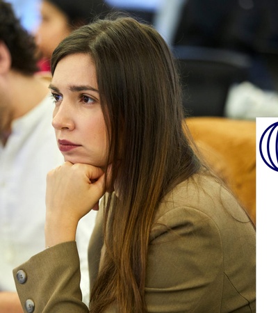 A woman in a business suit looks thoughtful while sitting at a meeting with other colleagues.