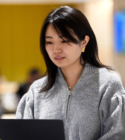 A woman works intently on a laptop in a busy office environment.