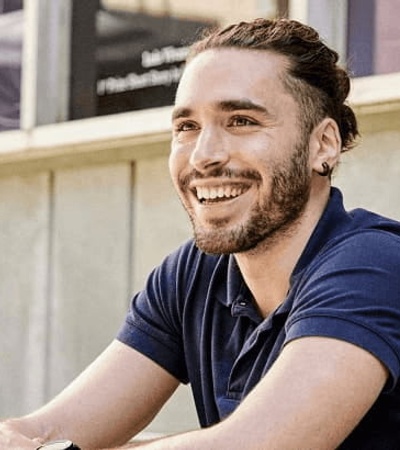 A man with a ponytail, smiling while using a laptop outdoors.