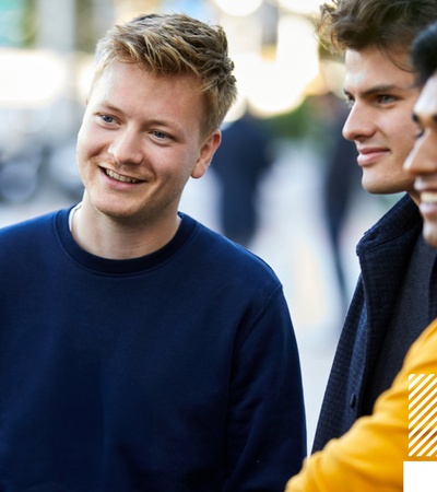 Three young men, smiling and engaging in a conversation on a city street.