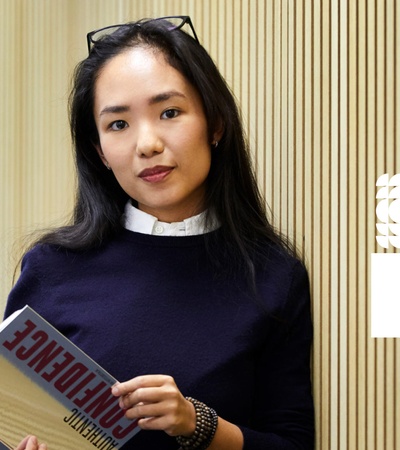 A woman holding a book titled 'ENGINEERING' stands in front of a modern patterned background.