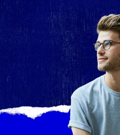 A young man with glasses is looking to the side against a blue background.