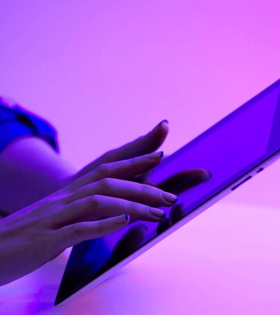 A person using a laptop in a room illuminated by purple light.