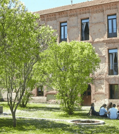 A group of people sitting on the grass near a building surrounded by trees.