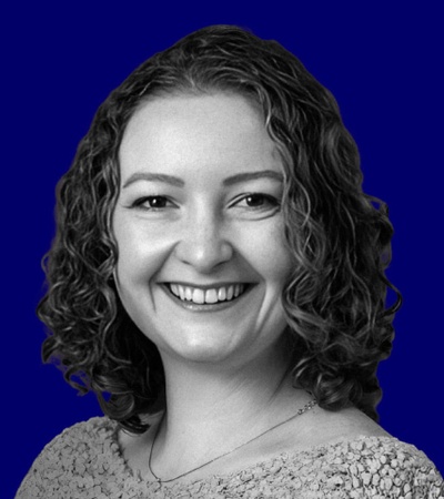 A grayscale image of a smiling woman with curly hair against a solid blue background.